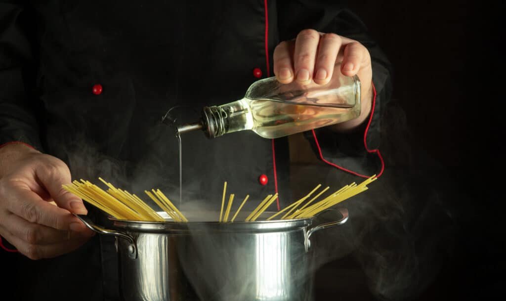 Professional chef adds konjac alcohol to a boiling pot of spaghetti. The idea of a delicious national Italian dish. Free space for recipe or menu on black background