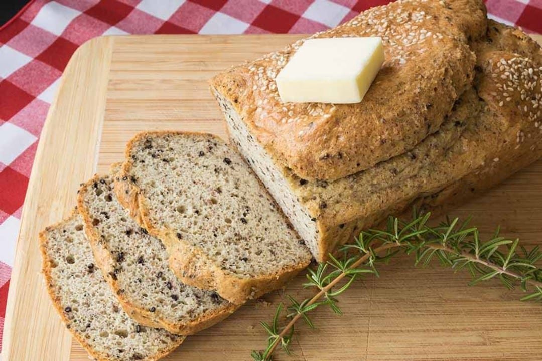 Sliced konjac bread with seeds and butter on a cutting board, garnished with rosemary.