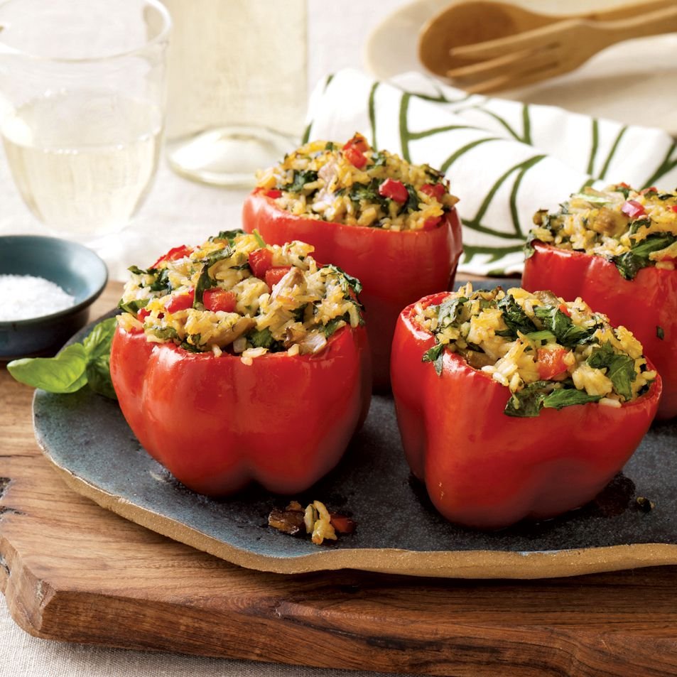 Four red bell peppers stuffed with a konjac rice, spinach, and mushroom mixture, baked and served on a blue plate.