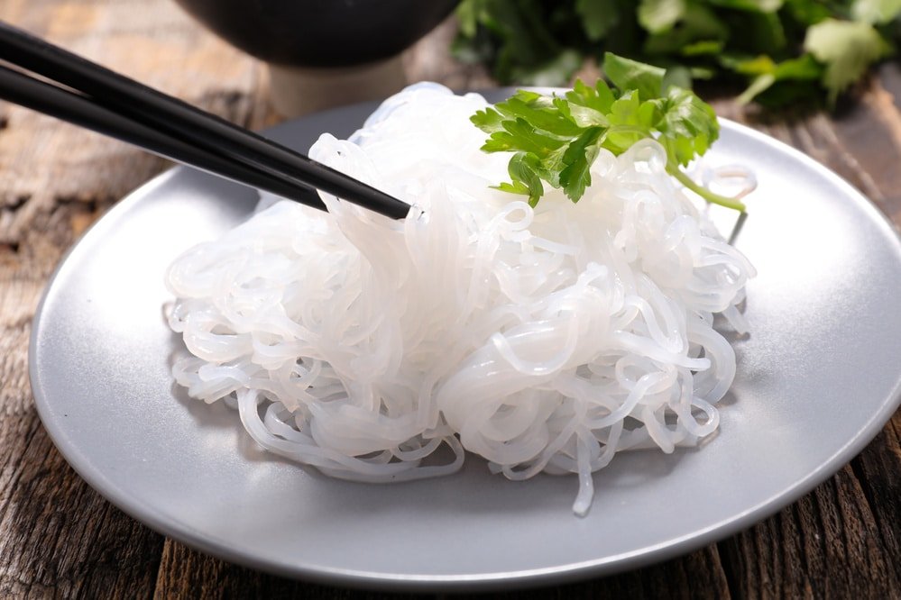 Plate of shirataki noodles (konjac noodles) with chopsticks and parsley garnish.