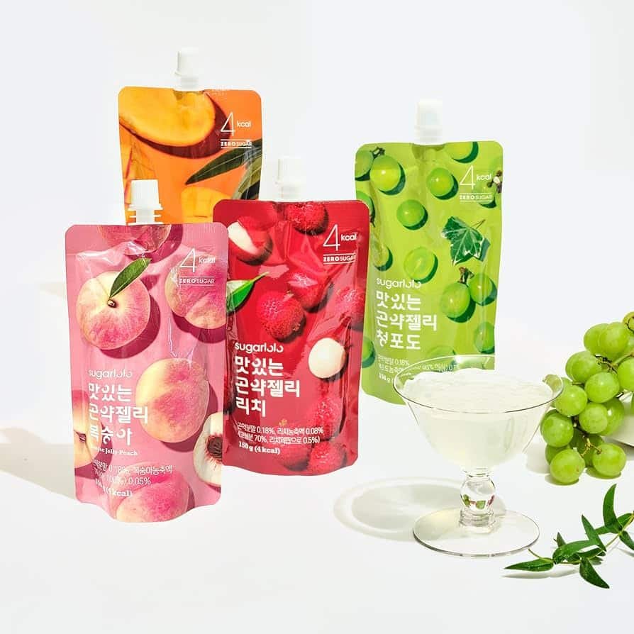 Four Sugarlolo drinkable konjac jelly pouches in peach, lychee, mango, and shine muscat flavors. A glass filled with shine muscat jelly and fresh grapes are beside the pouches.