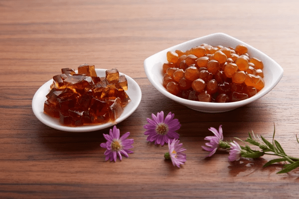 Two white bowls on a wooden table: one with cubes of konjac jelly, the other with tapioca pearls.