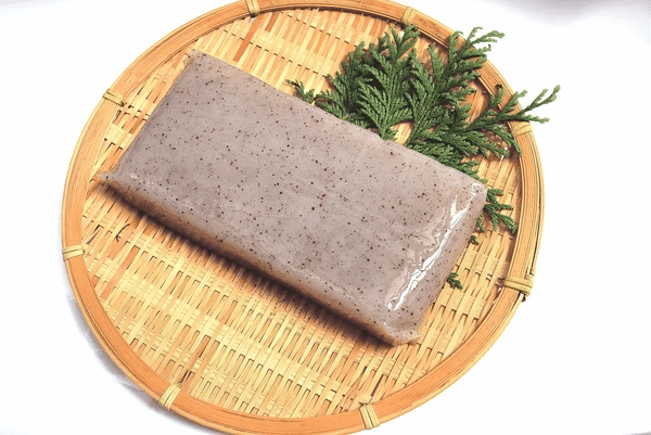 What is konjac jelly? A rectangular block of konjac, packaged in plastic, rests on a circular woven bamboo tray with a small sprig of green leaves.