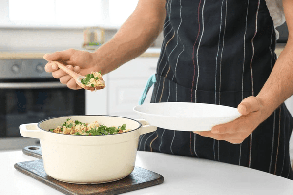 Person serving cooked rice from a pot onto a plate.