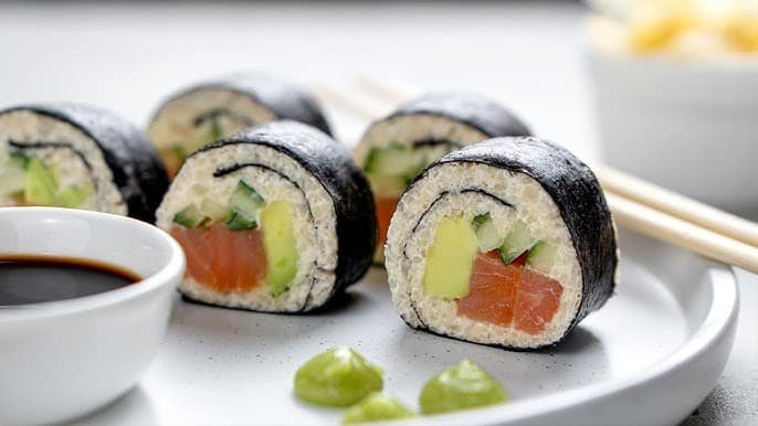 Keto sushi rolls with salmon, avocado, and cucumber on a white plate with soy sauce and wasabi.